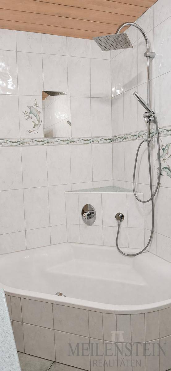 Eckbadewanne mit integrierter Duschfunktion und hellen Fliesen, die ein sauberes Ambiente schaffen.