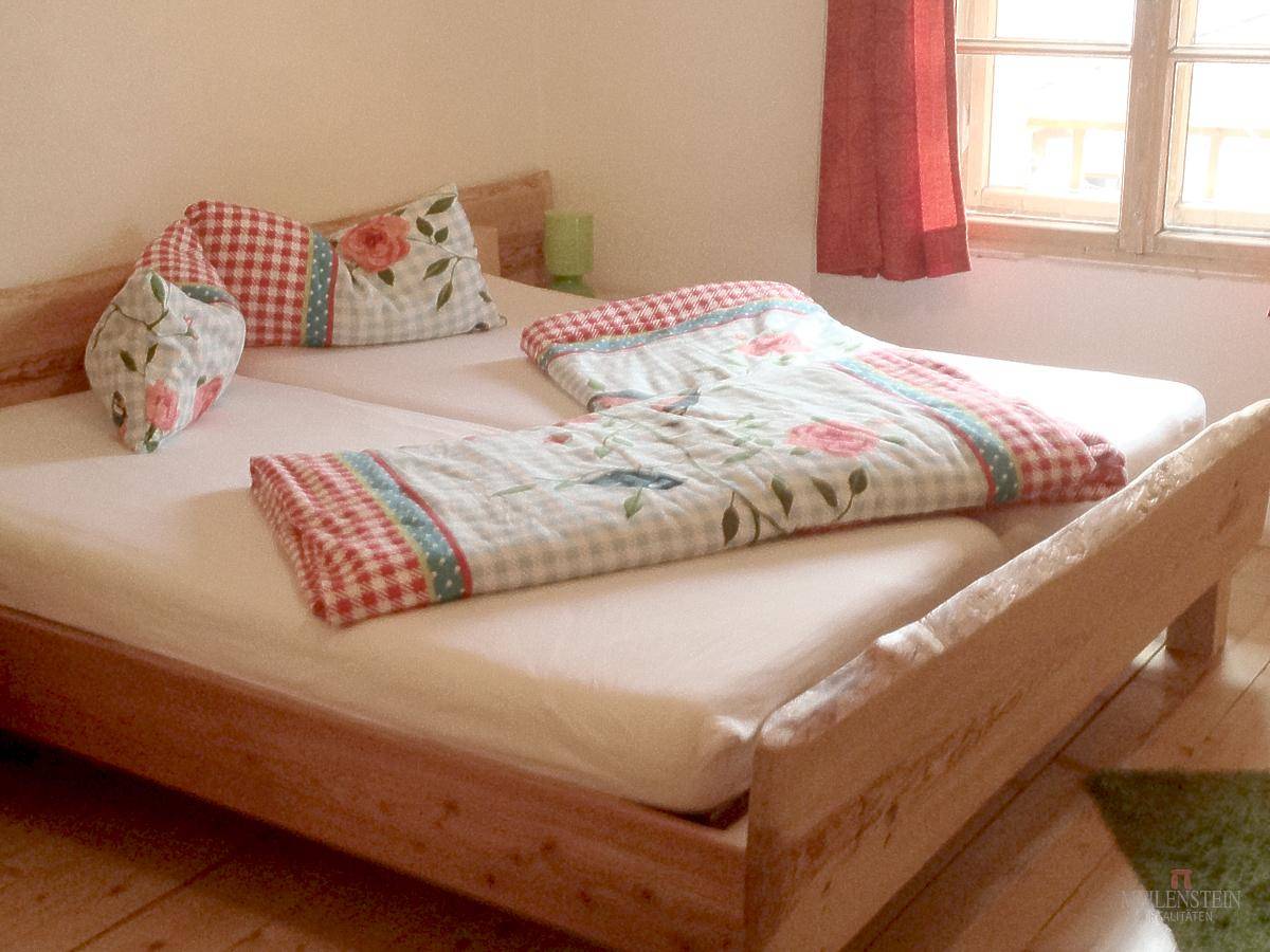 Helles Schlafzimmer mit zwei Einzelbetten, Holzboden und Fenster mit Blick nach draußen.