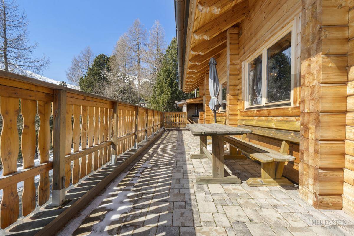 Langer Holzbalkon mit Sitzgelegenheiten und Blick auf die verschneite Landschaft.