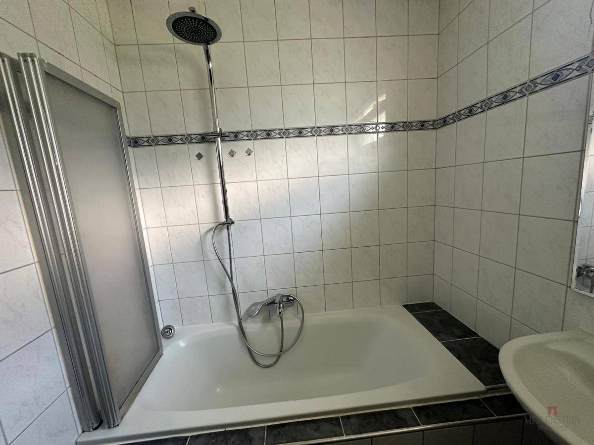 Badezimmer mit Badewanne, Duschkopf und Waschbecken, ausgestattet mit älteren Fliesen.