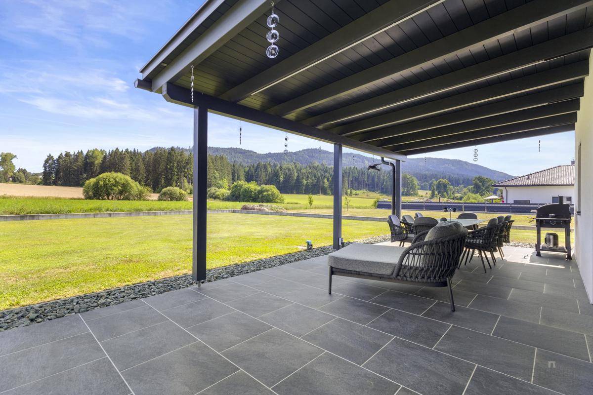 Geräumige, überdachte Terrasse mit modernen Gartenmöbeln und weitem Blick ins Grüne.