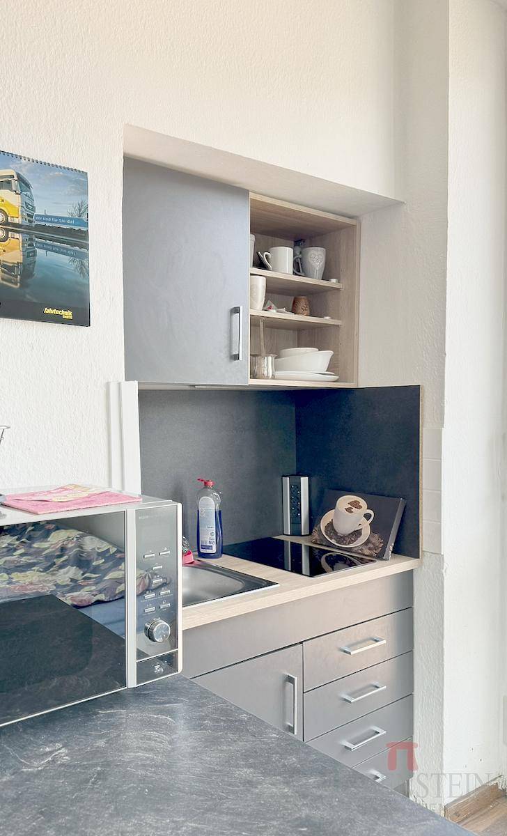 Kleine, kompakte Küchenzeile mit Spüle, Kochfeld und Mikrowelle in einem Nischenbereich.