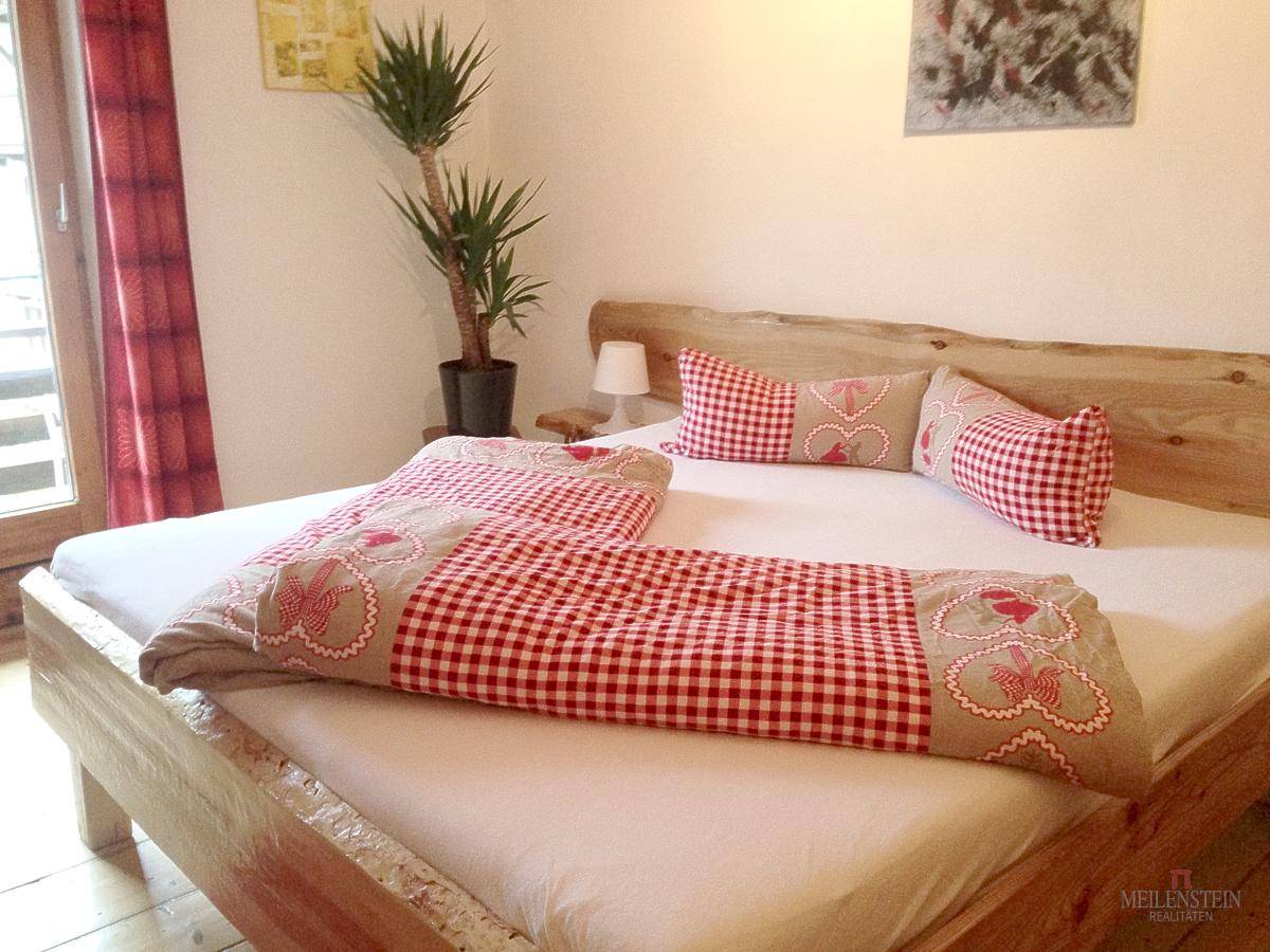Helles Schlafzimmer mit Holzbett, karierter Bettwäsche und Balkonzugang.