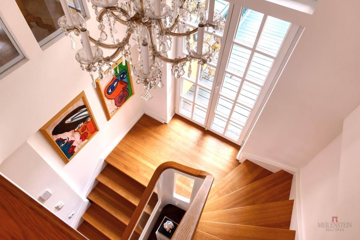 Elegantes Treppenhaus mit Holzstufen, Glasgeländer und Kronleuchter.