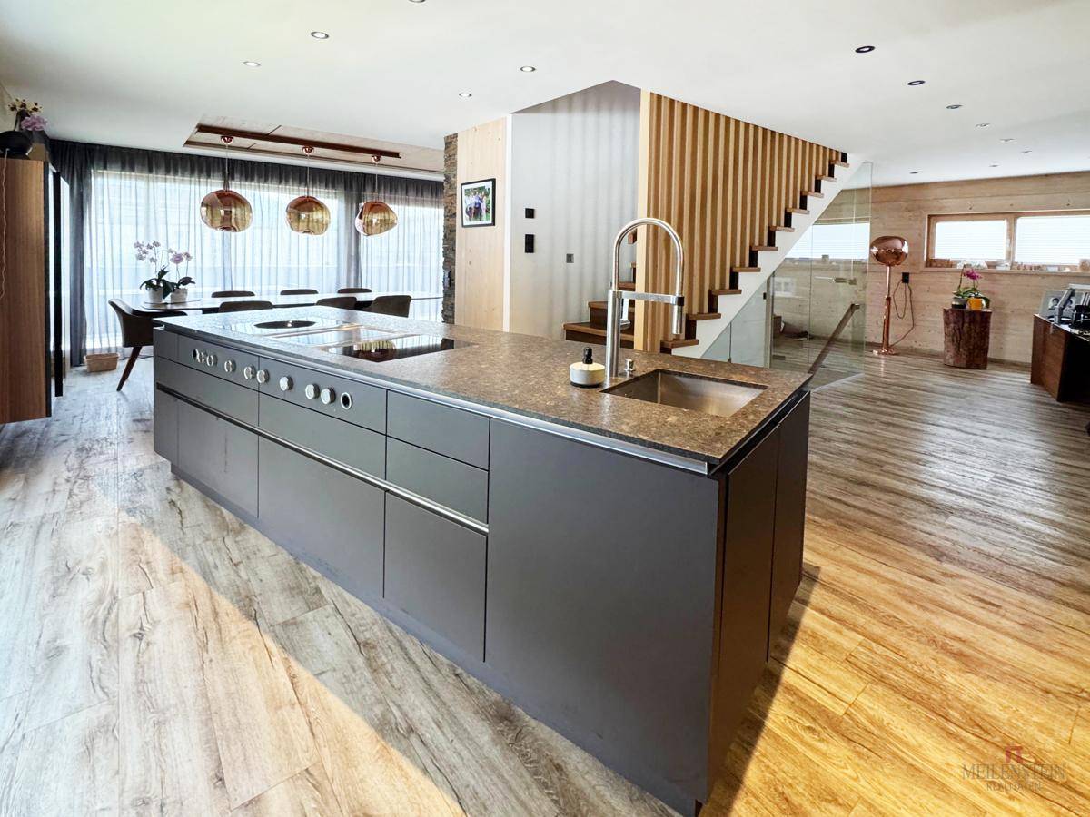 Offene Küche mit großer Kochinsel und Essbereich, verbunden durch eine elegante Holztreppe.