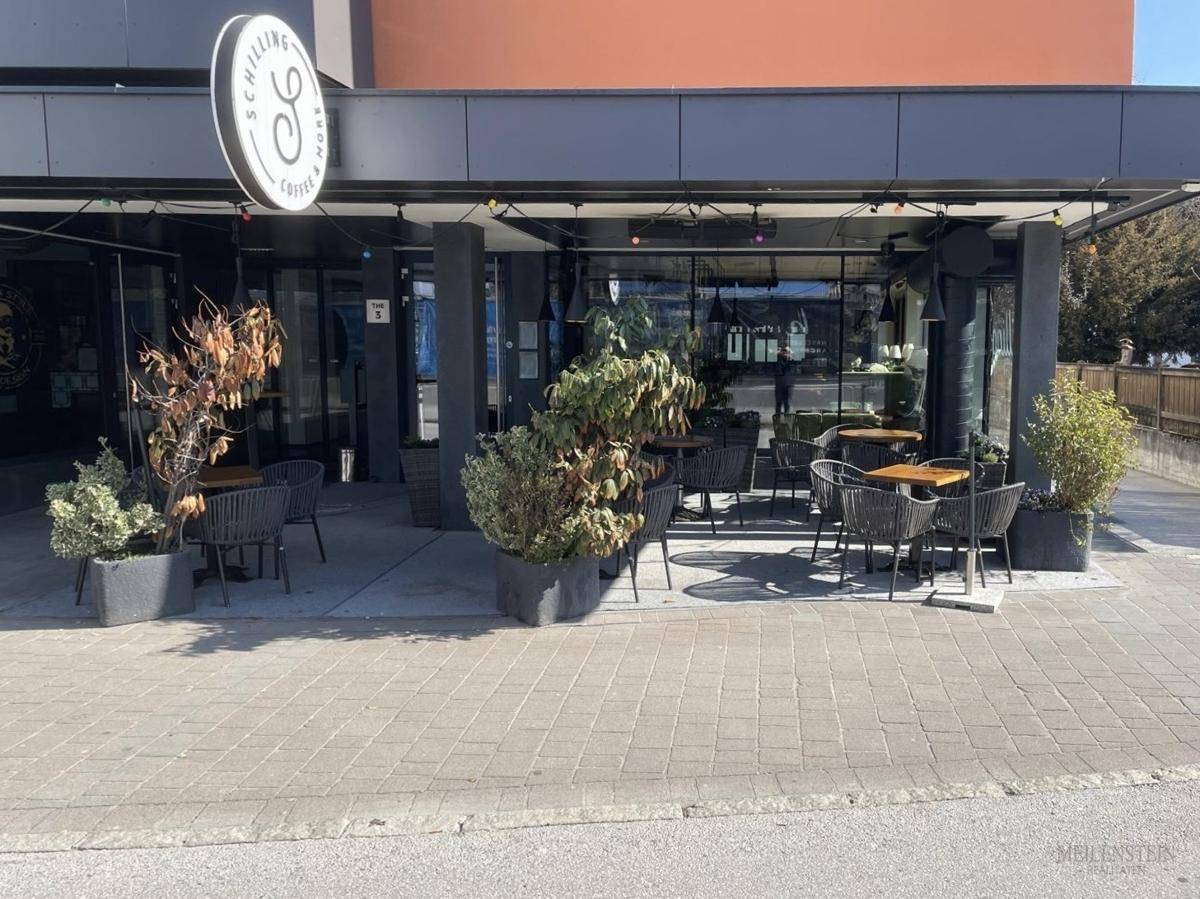 Außenbereich des Cafés mit Tischen und Stühlen auf dem Bürgersteig, umgeben von Pflanzen.