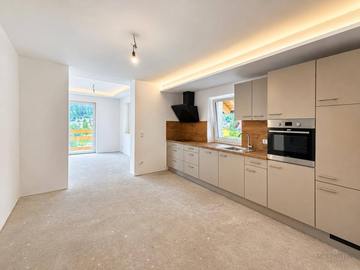 Moderne Einbauküche mit beigen Fronten und Holzakzenten, ausgestattet mit Backofen, in einem noch unfertigen Raum.