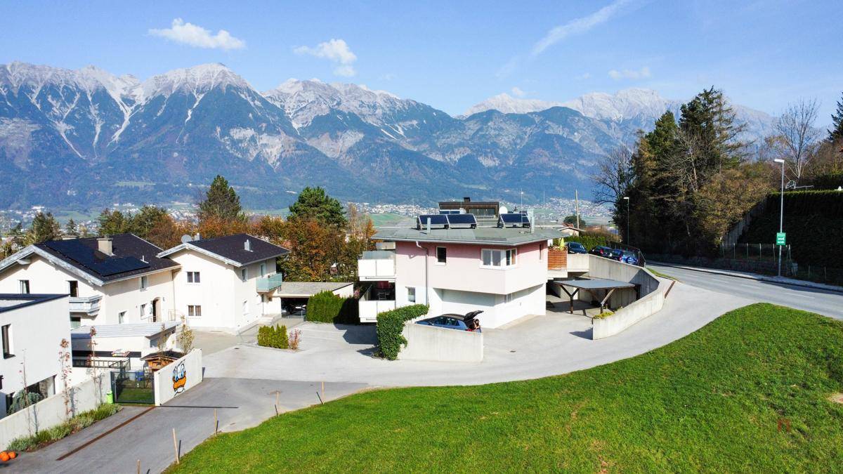 Wohngebäude mit Photovoltaikanlage, umgeben von Grünflächen und mit Panoramablick auf die schneebedeckten Berge.