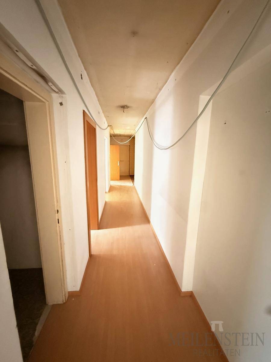 Langer Flur mit Linoleumboden und weißen Wänden, der Renovierungsbedarf aufweist.