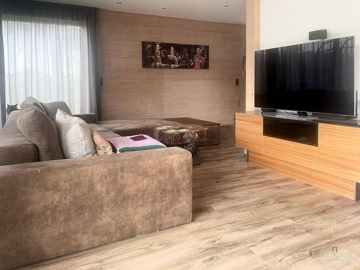 Geräumiges Wohnzimmer mit großem Sofa, Holzboden und Medienmöbeln in warmem Ambiente.