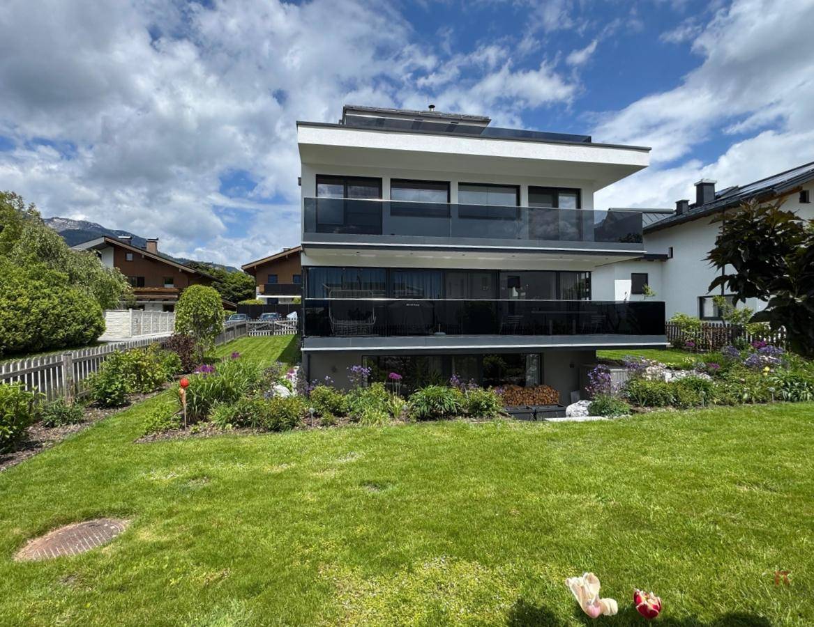 Gesamtansicht des modernen Hauses mit großem Garten und mehreren Balkonen unter bewölktem Himmel.