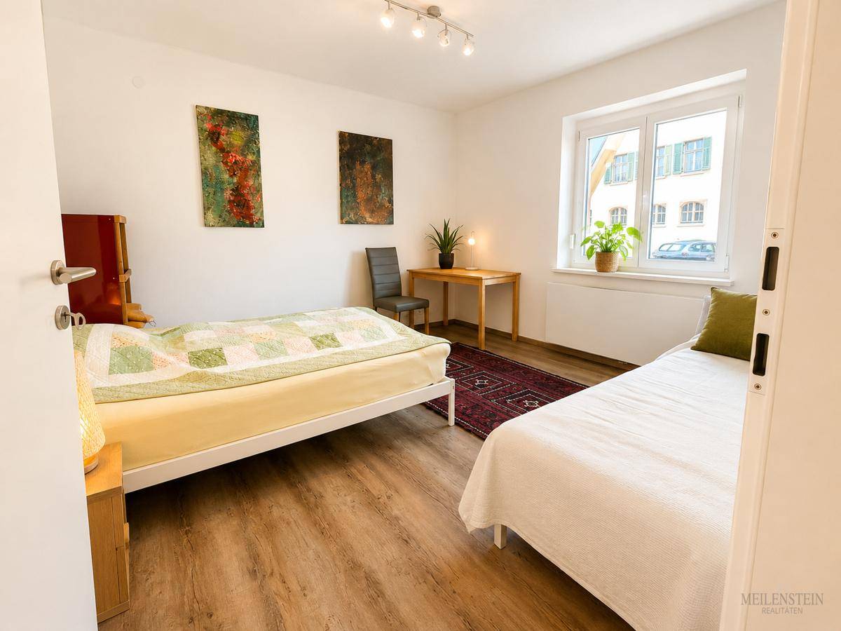 Helles Schlafzimmer mit zwei Einzelbetten, Holzboden und Fenster mit Blick nach draußen.