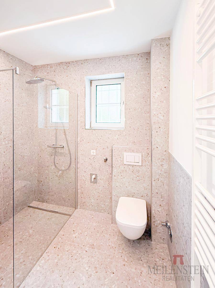 Modernes Badezimmer mit begehbarer Dusche, wandhängendem WC, hellen Fliesen und Fenster.
