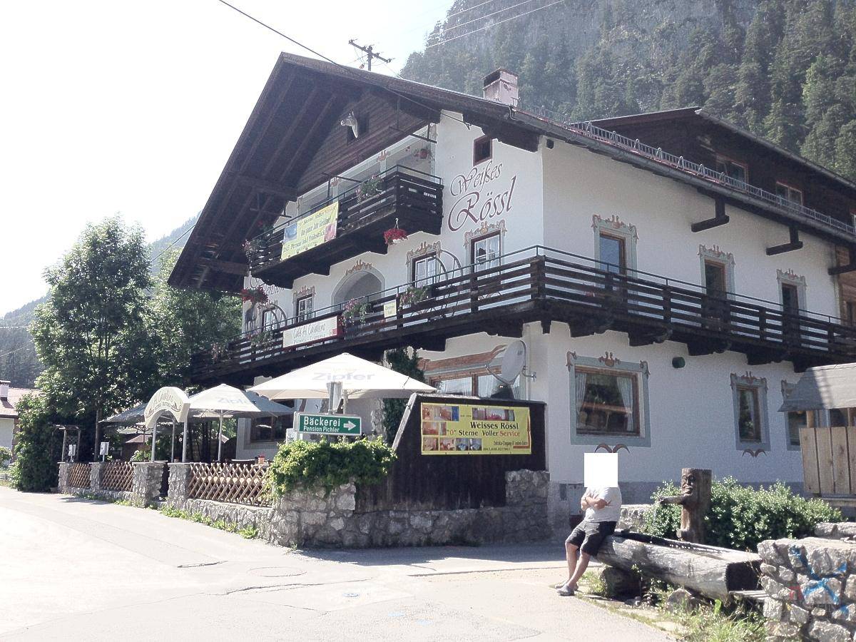 Alpines Gasthaus mit Balkonen und Außenterrasse an einem sonnigen Sommertag.