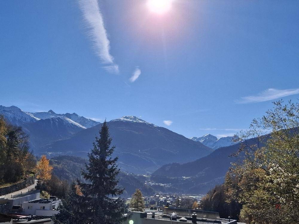Panoramablick über ein sonniges Tal mit einer Stadt und majestätischen Bergen im Hintergrund.