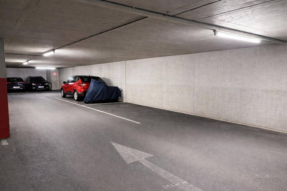 Geräumige Tiefgarage mit mehreren geparkten Autos und klaren Fahrbahnmarkierungen auf dem Boden.