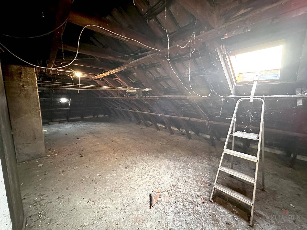 Unausgebauter Dachboden mit sichtbarer Holzkonstruktion, Dachfenster und einer Leiter.