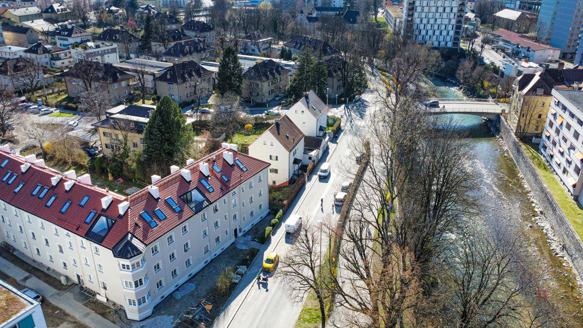 Luftaufnahme einer Stadtstraße mit Wohngebäuden, Fluss und Bergen in der Ferne.