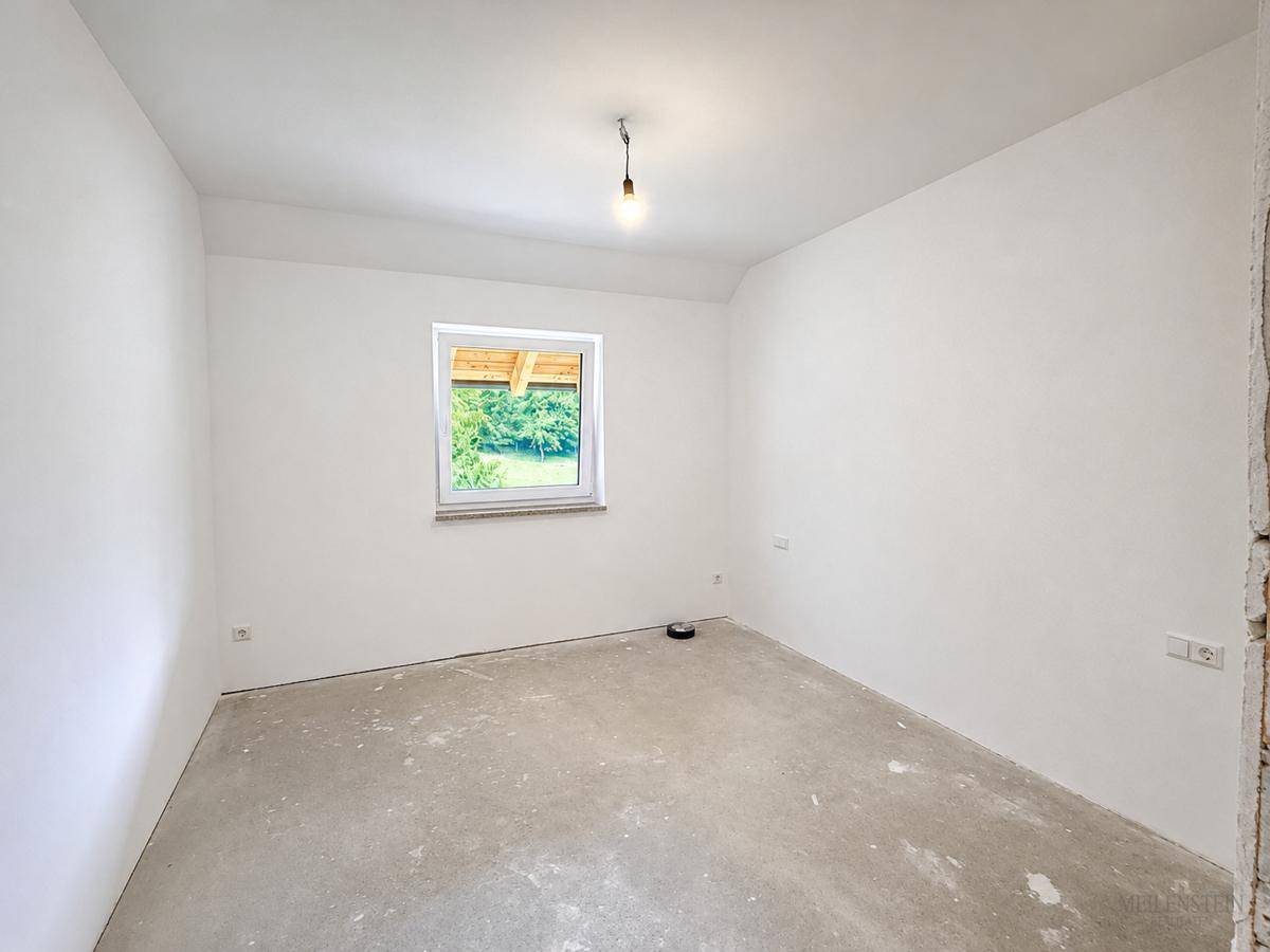 Leeres Zimmer mit Betonboden und weißen Wänden, bietet viel Potenzial für individuelle Gestaltung.