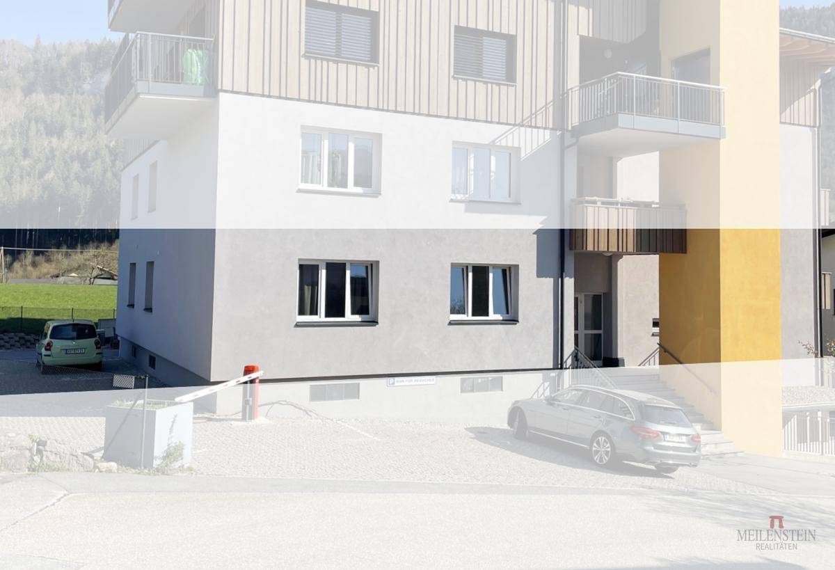 Fassade eines modernen Mehrfamilienhauses mit Balkonen und Parkplätzen im Vordergrund.