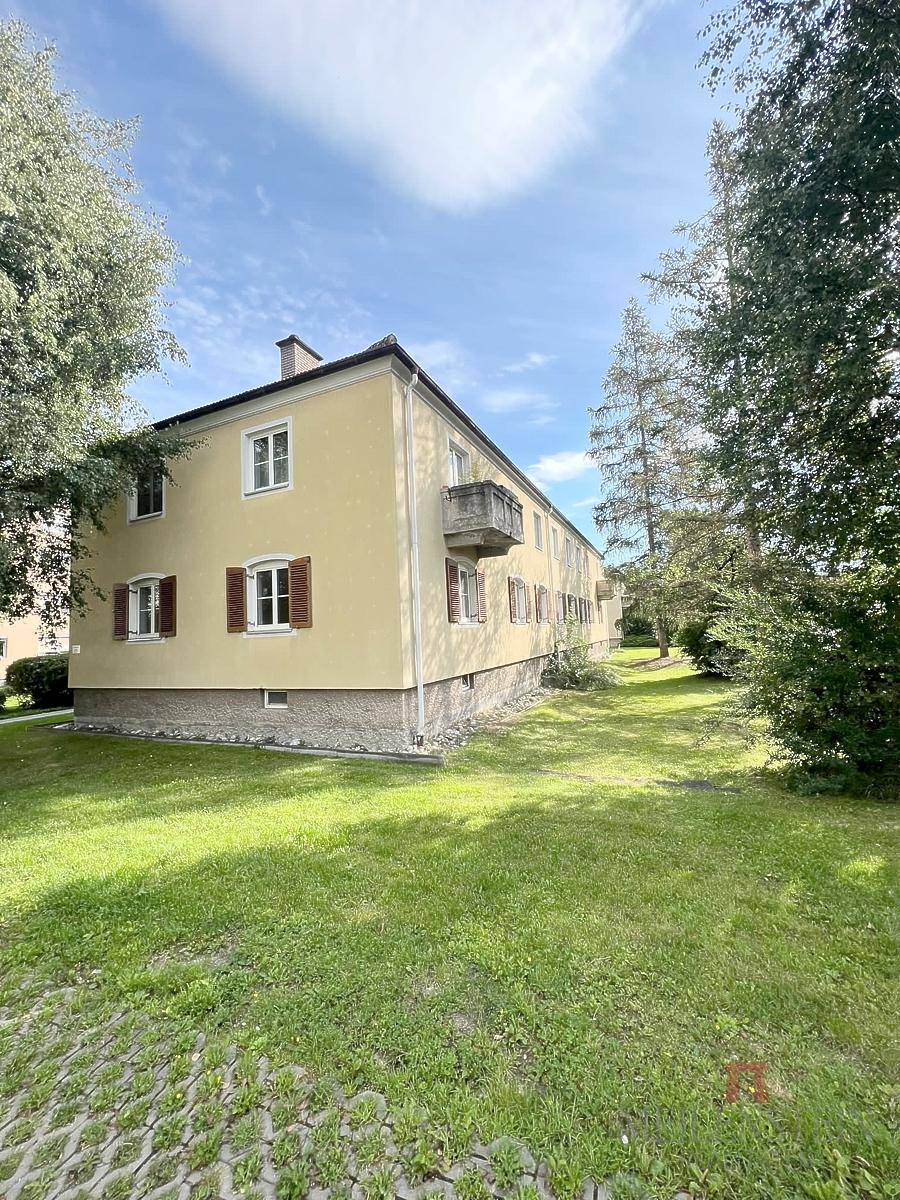 Seitenansicht des Mehrfamilienhauses mit einem kleinen Balkon und weitläufiger Grünfläche.