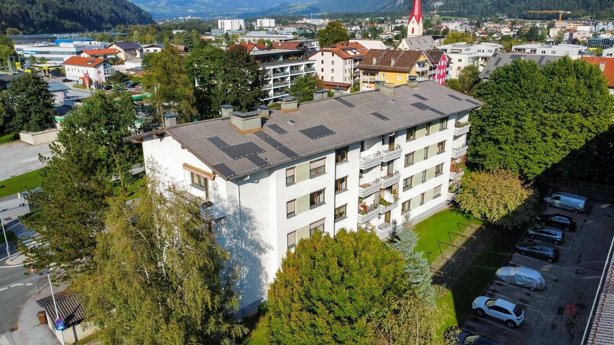 Luftaufnahme eines Mehrfamilienhauses mit Satteldach und umliegenden Bäumen.
