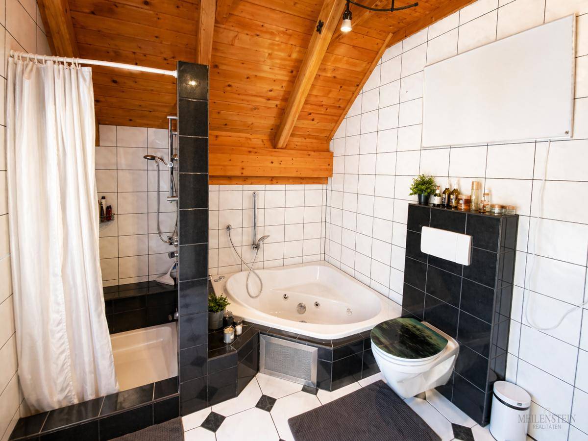 Badezimmer mit Eckbadewanne, Dusche und schwarz-weißen Fliesen unter Holzdachschräge.