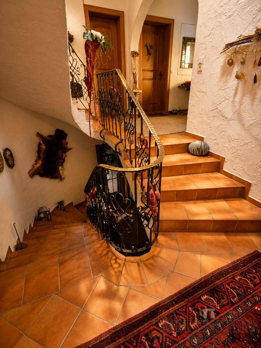 Elegantes Treppenhaus mit geschwungener Treppe, schmiedeeisernem Geländer und Terrakotta-Fliesen.