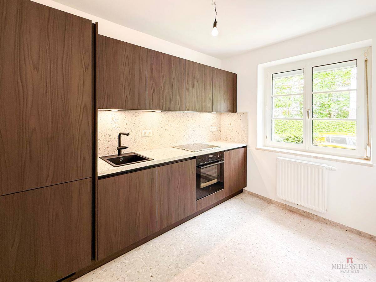 Moderne Küche mit dunklen Holzschränken, heller Arbeitsplatte, integrierten Geräten und Fenster.