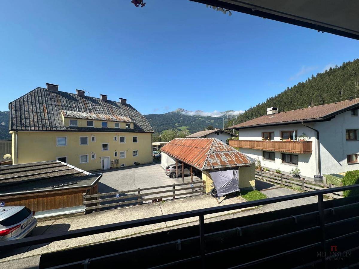 Blick vom Balkon auf umliegende Häuser und die grüne Berglandschaft in der Ferne.