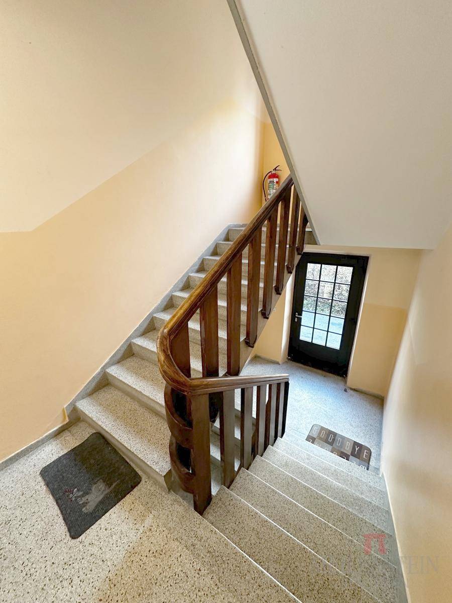 Treppenhaus mit Terrazzostufen und einem klassischen Holzgeländer in einem Mehrfamilienhaus.