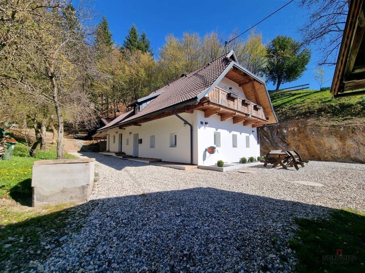 Charmantes Landhaus mit weißer Fassade, Holzbalkonen und Kiesauffahrt in grüner Umgebung.