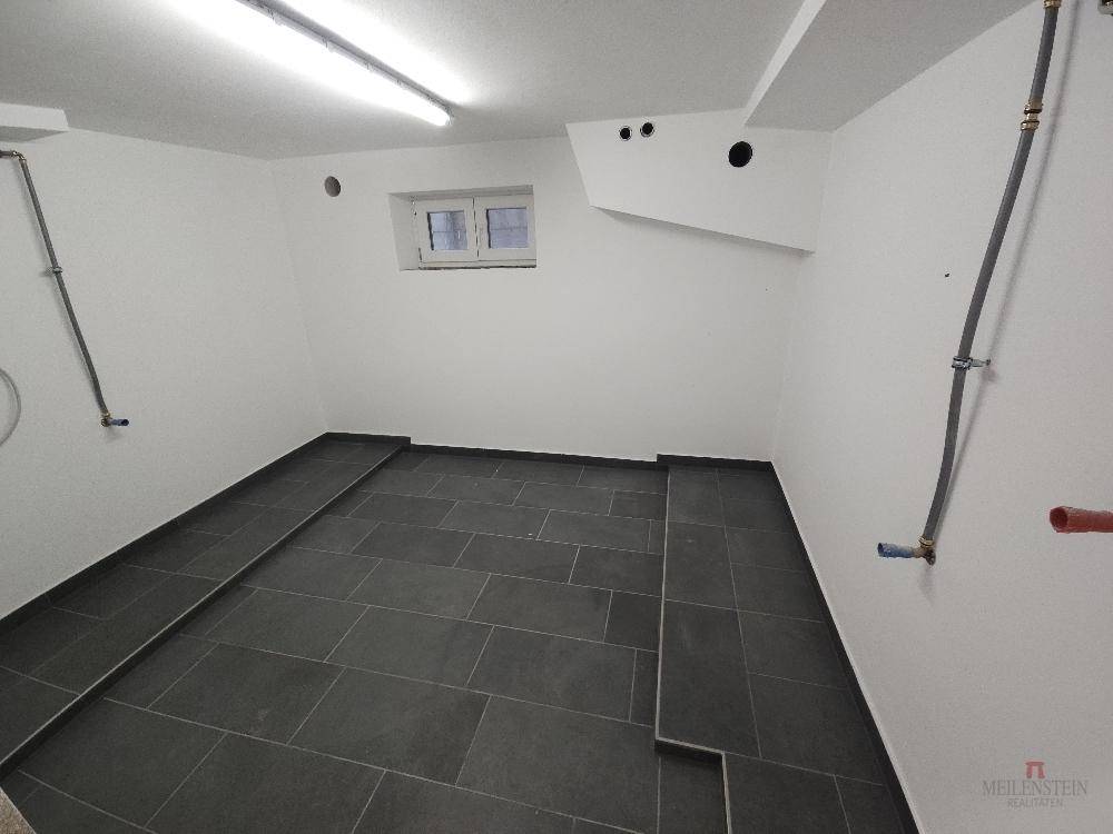 Kellerraum mit Fliesenboden und kleinem Fenster, ideal als Waschküche oder Abstellraum.