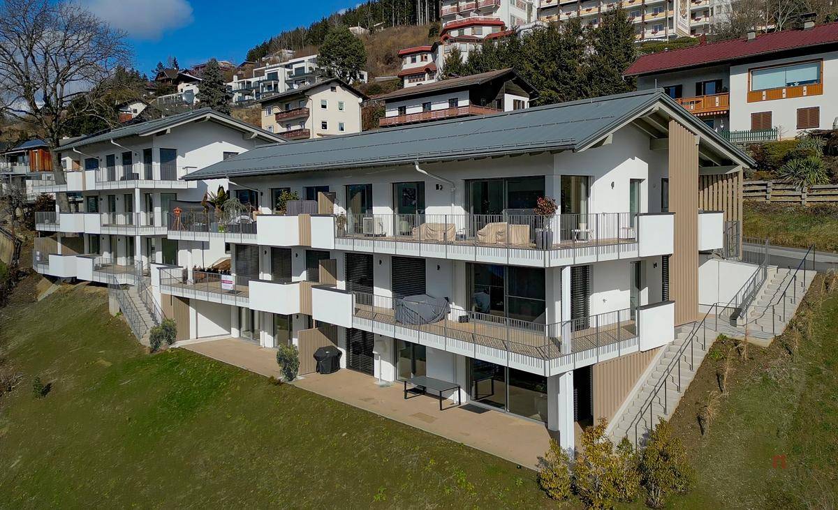 Moderne Wohnanlage am Hang mit mehreren Balkonen und Terrassen, umgeben von Natur.