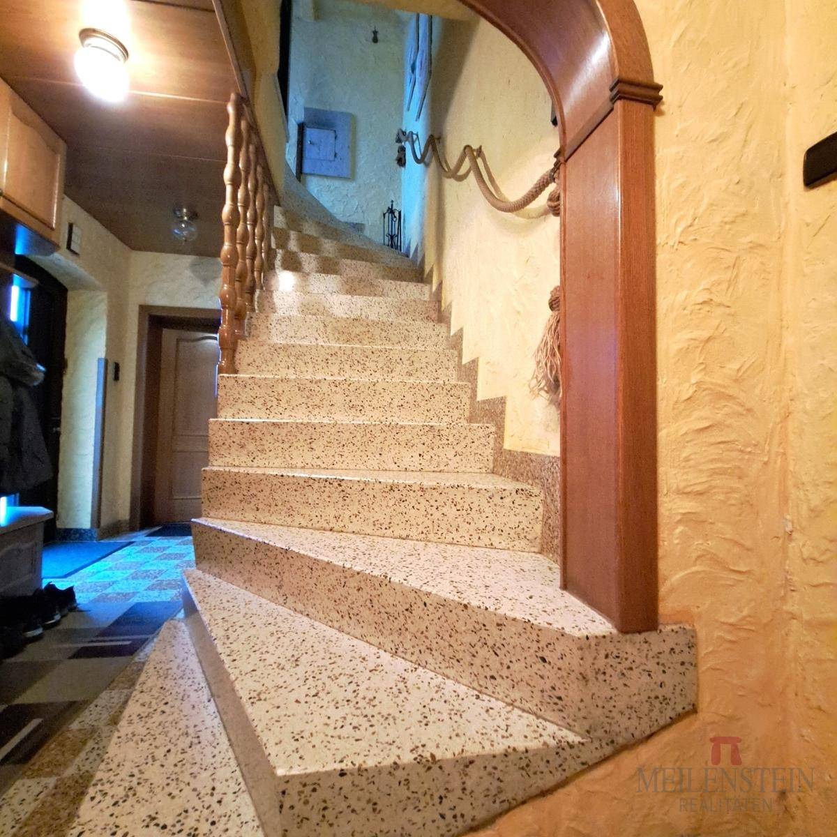 Geschwungene Treppe mit Terrazzostufen und Holzgeländer in einem traditionellen Flur.