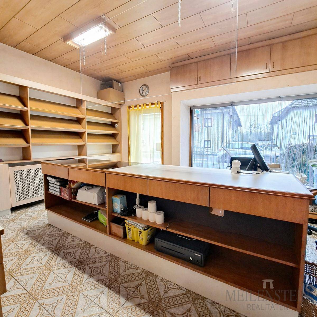 Raum mit großem Tresen, Holzregalen und einem Fenster, ideal als Büro oder Ladenfläche nutzbar.