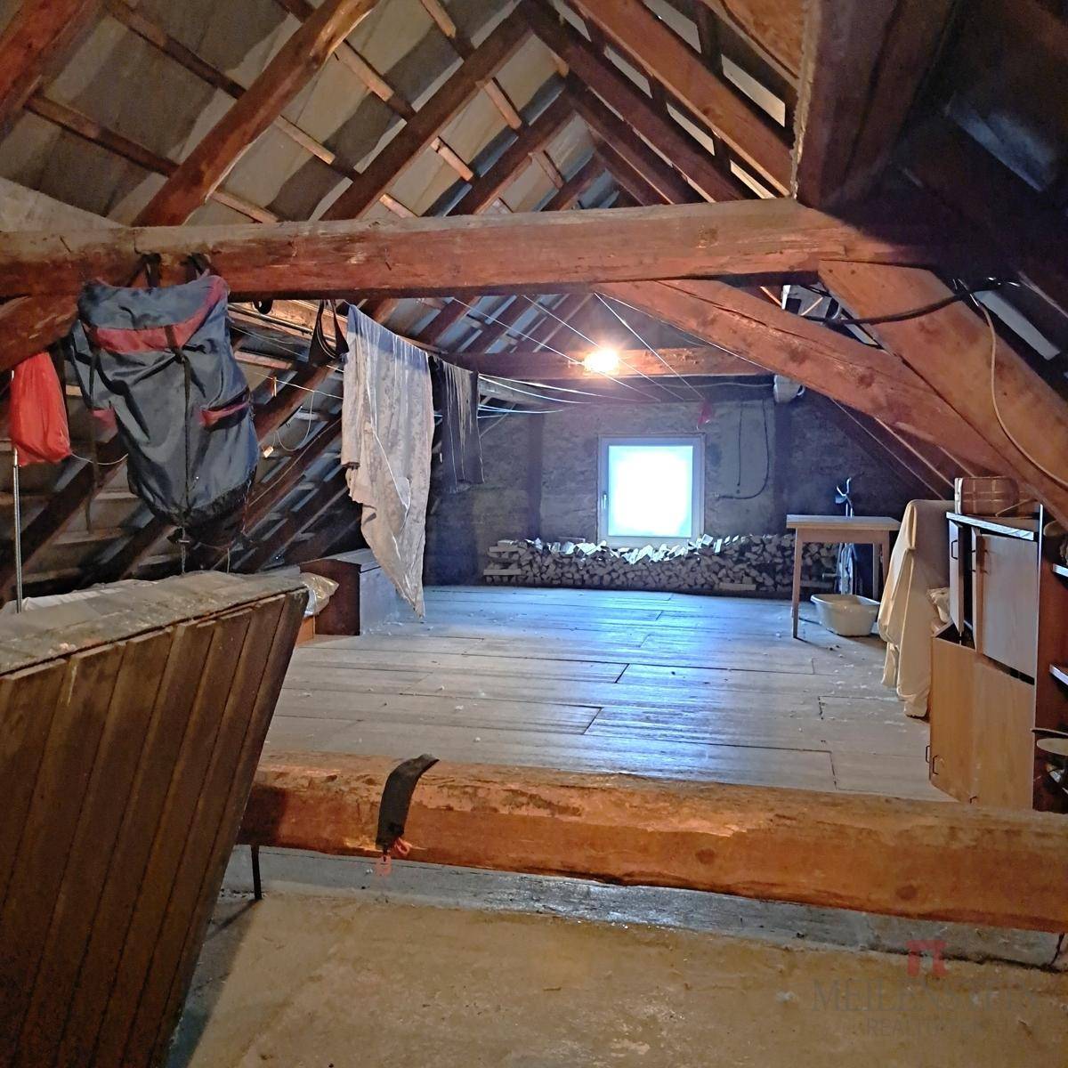 Unausgebauter Dachboden mit sichtbaren Holzbalken, Holzfußboden und kleinem Fenster.