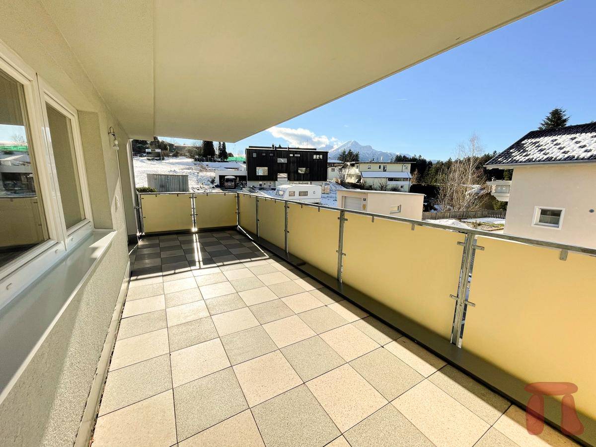 Breiter Balkon mit Fliesenboden, Sichtschutz und weitem Blick auf die Berglandschaft.