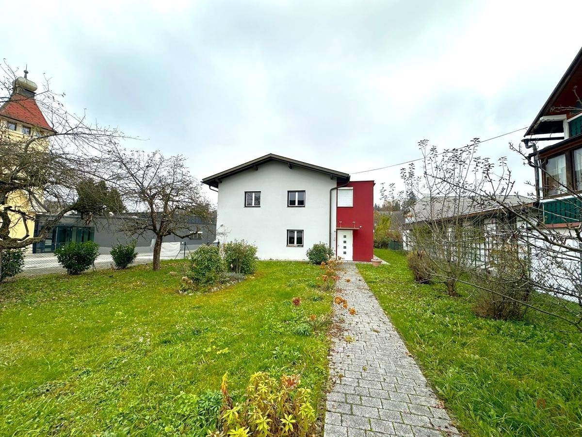 Frontansicht eines modernen Hauses mit weißer und roter Fassade und gepflegtem Vorgarten.