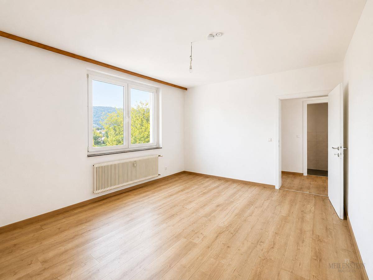 Helles Zimmer mit Laminatboden und einem Fenster, das einen Blick ins Grüne bietet.