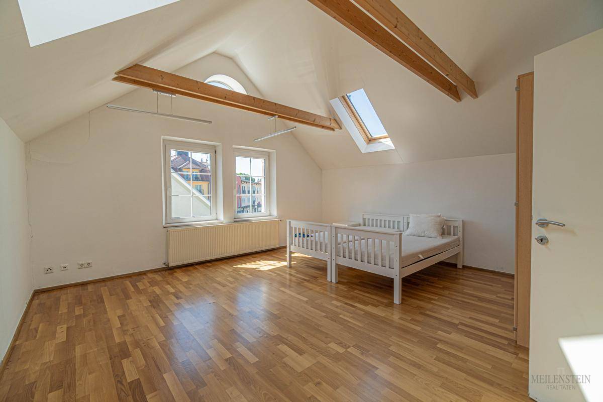 Helles Schlafzimmer im Dachgeschoss mit Holzboden, sichtbaren Holzbalken und Dachfenstern.