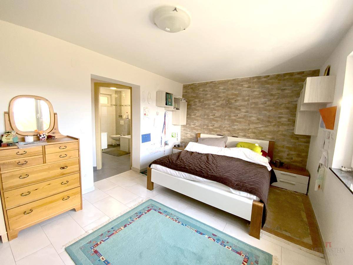 Schlafzimmer mit Doppelbett, Steinwandakzent und direktem Zugang zu einem Badezimmer.
