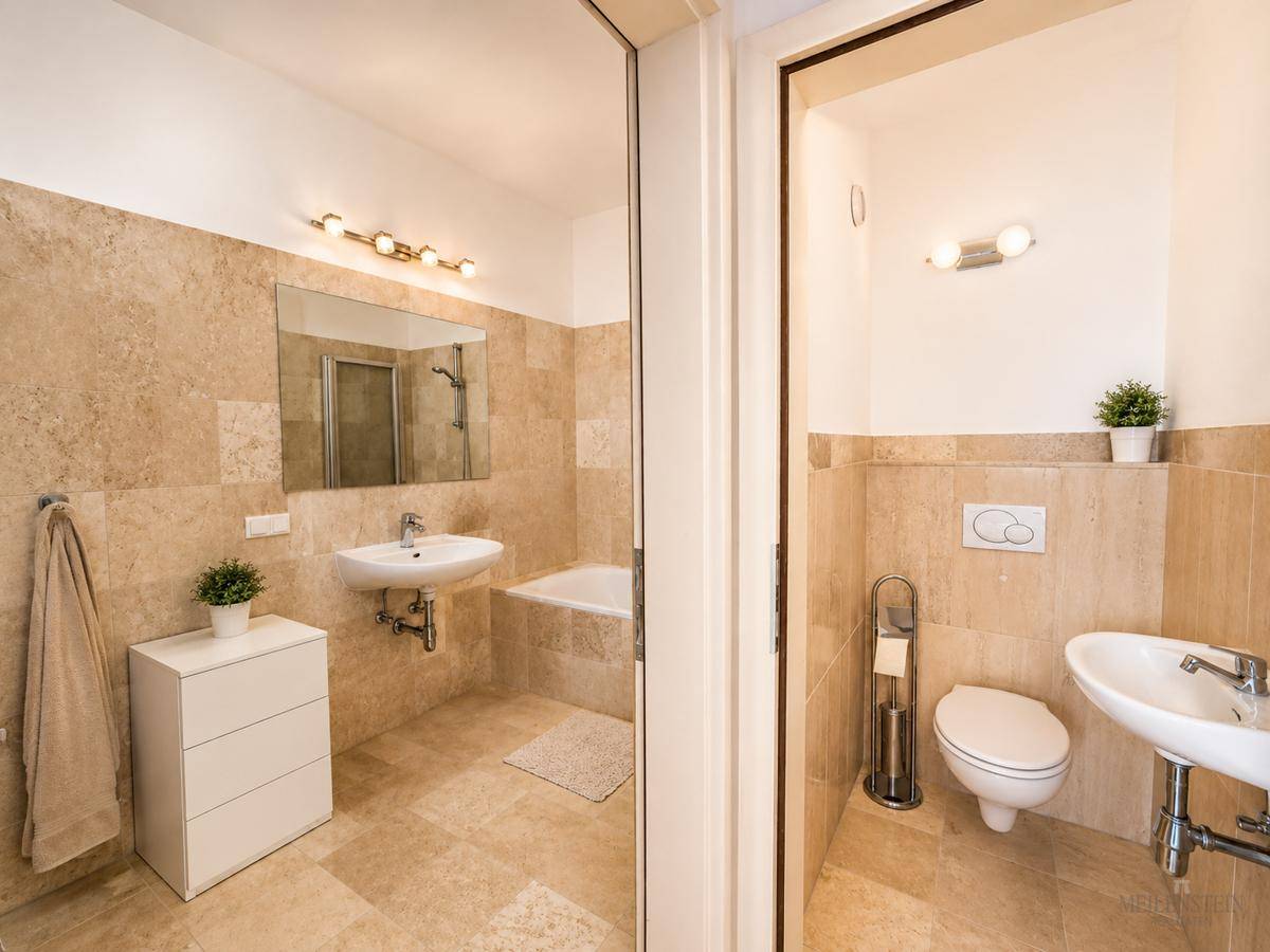 Modernes Badezimmer mit beigefarbenen Fliesen, Waschbecken, Badewanne und separatem WC-Bereich.