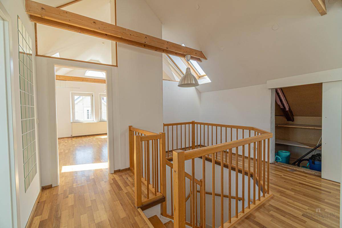 Helles Treppenhaus im Dachgeschoss mit Holzgeländer und Dachfenstern, die den Bereich erhellen.