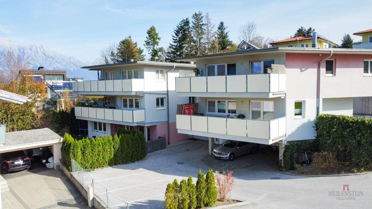 Zwei moderne Wohngebäude mit Balkonen, Carports und einem schönen Blick auf die umliegende Berglandschaft.