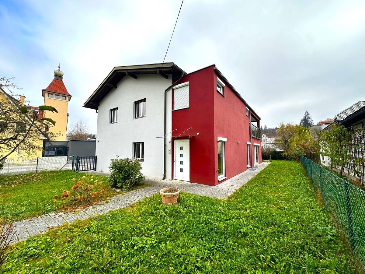 Modernes Einfamilienhaus mit weißer und roter Fassade, umgeben von einem grünen Garten.