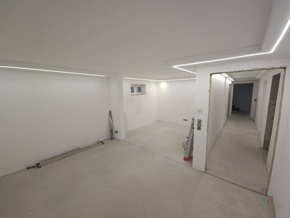 Geräumiger Kellerbereich im Rohbau mit moderner Deckenbeleuchtung und Zugang zu weiteren Räumen.