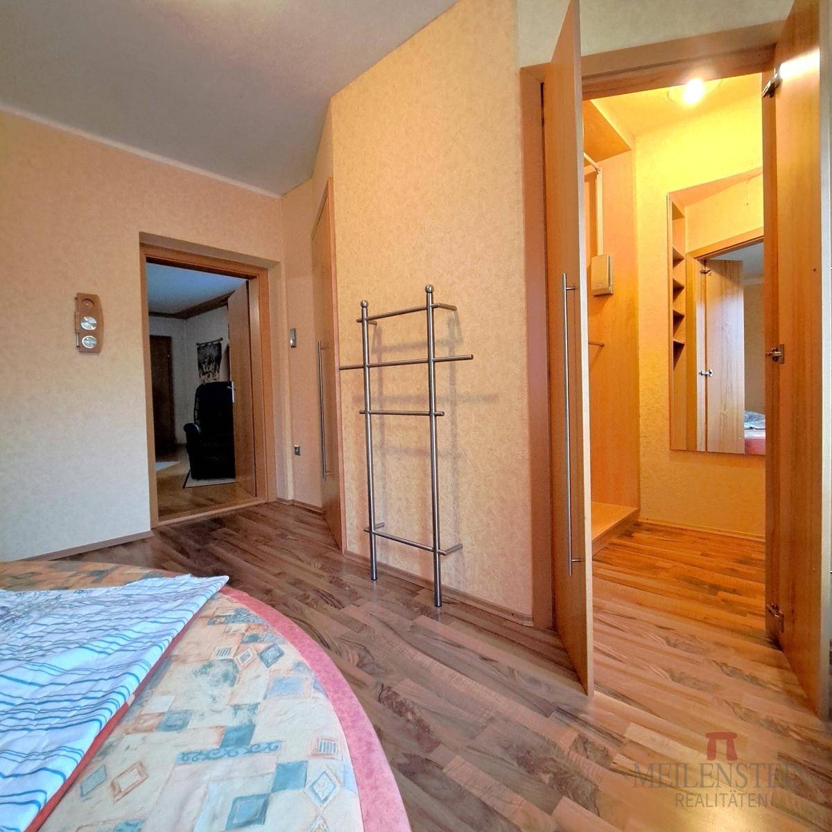 Schlafzimmer mit Laminatboden und offenem Zugang zu einem begehbaren Kleiderschrank.