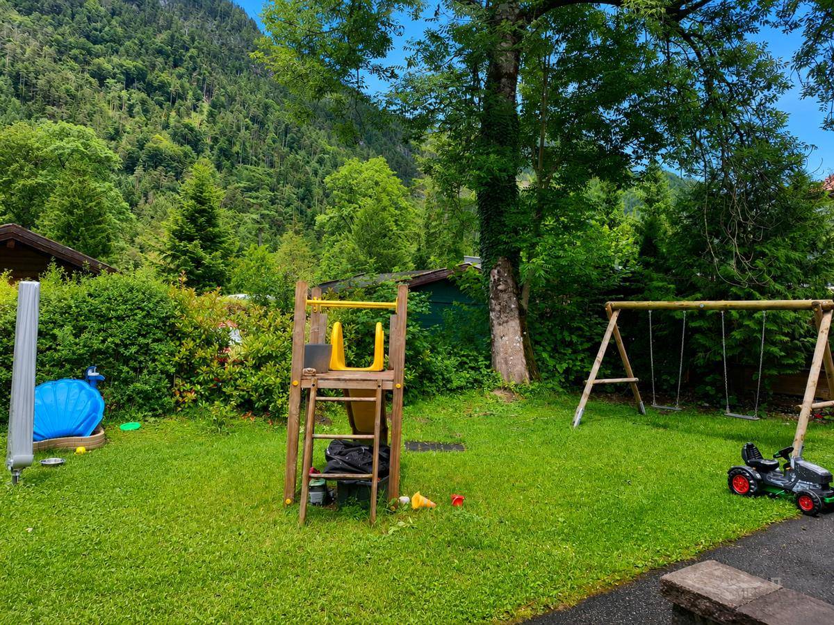 Grüner Gartenbereich mit Rasenfläche, Spielgeräten und umgeben von Bäumen und Natur.