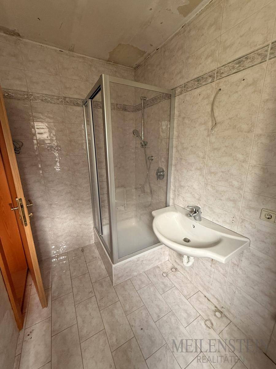 Gefliestes Badezimmer mit Duschkabine und Waschbecken, das eine Modernisierung benötigt.